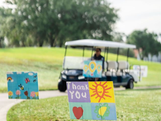 Golf cart in background, with a forefront sign made by a child saying thank you.